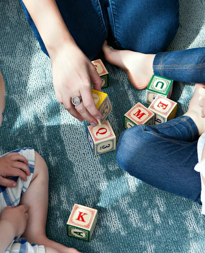 Two toddlers playing with alphabet blocks on the floor