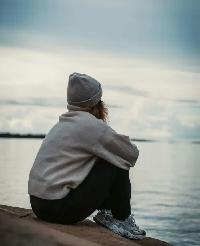 A young person sitting alone by the water, deep in thought